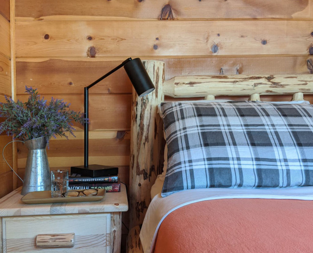 Wood bed in cabin with bedside table and plaid pillow